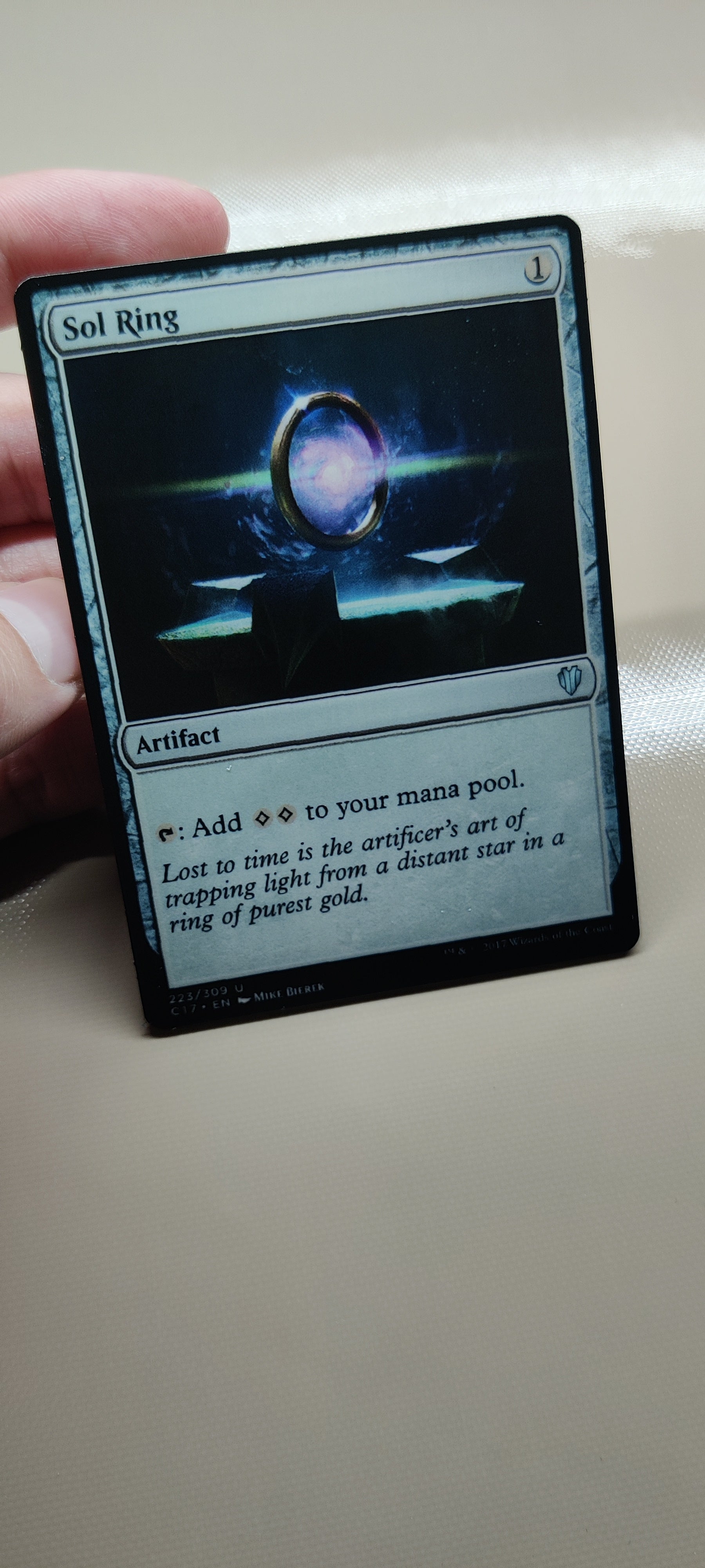 Hand holding a collectible card with 'Sol Ring' on a plain background. Magic the gathering sol ring proxy card on metal blank